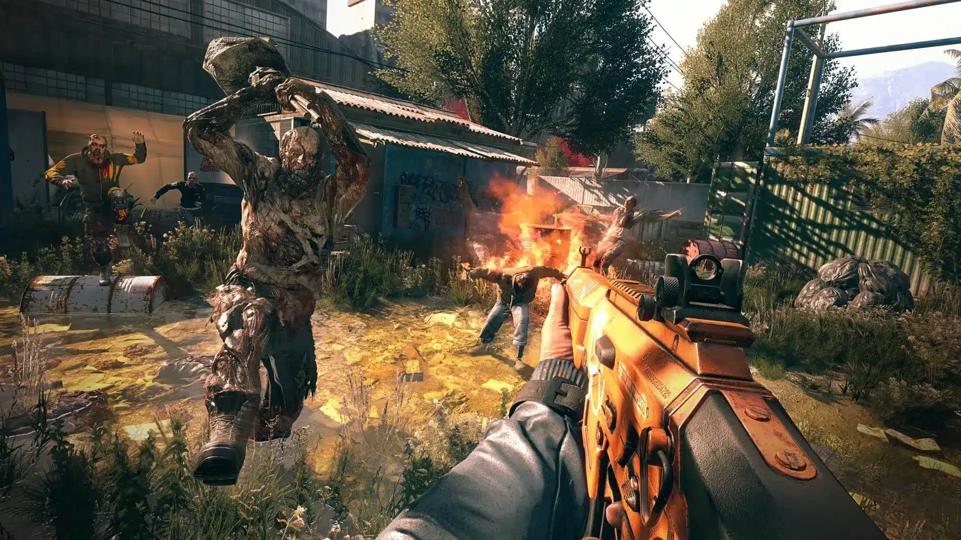 First-person perspective of a player holding an orange assault rifle facing several zombies in an urban ruin