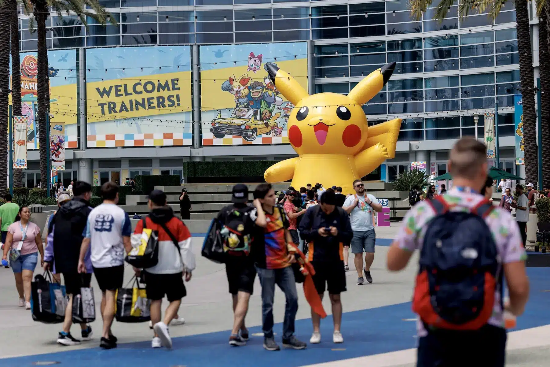 Giant inflatable Pikachu in front of a convention center with 'Welcome Trainers!' signage and crowds of people.