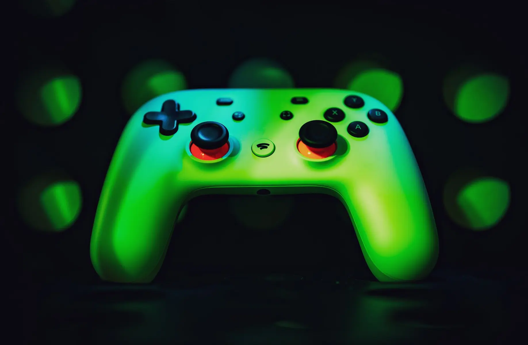 A white Google Stadia controller illuminated with green light against a dark bokeh background
